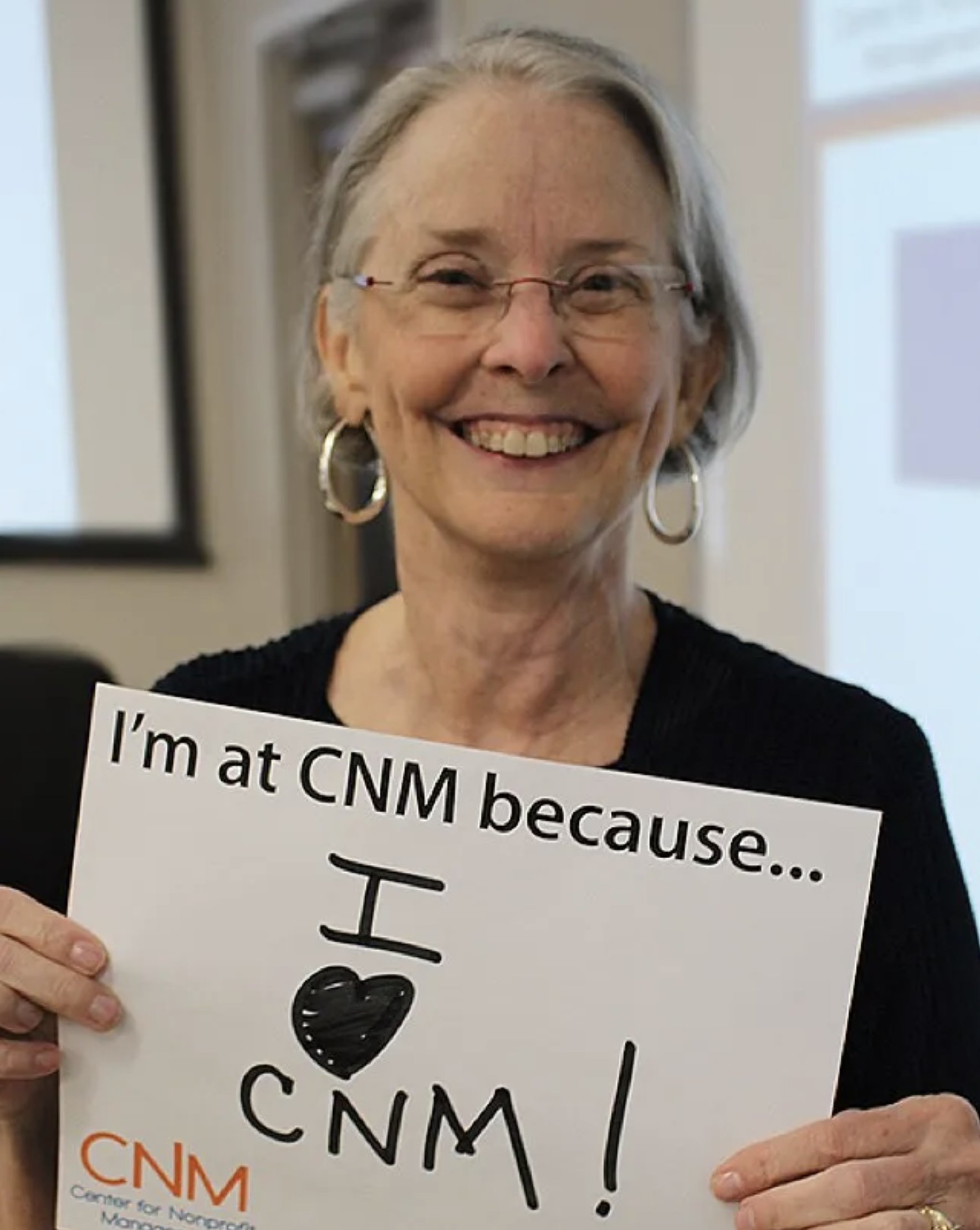 Nonprofit employee smiling and holding a sign " I'm at CNM because I love CNM"